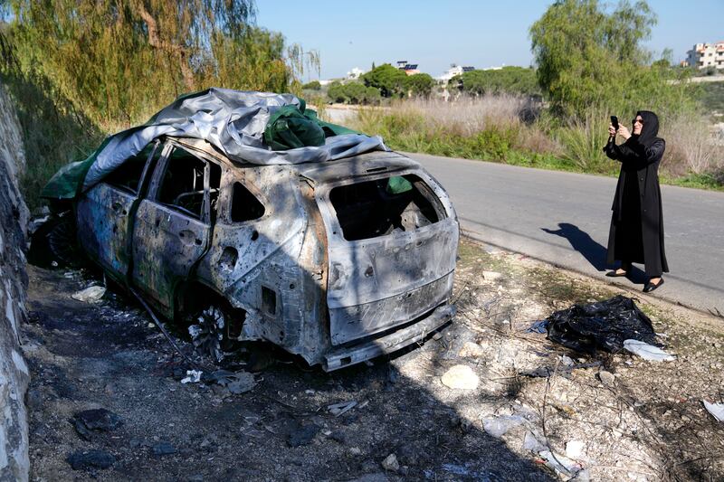 A woman takes pictures of a burned car used by the senior Hezbollah commander Wissam Tawil, who was killed on Monday, in Kherbet Selem village, south Lebanon (Hussein Malla/AP)