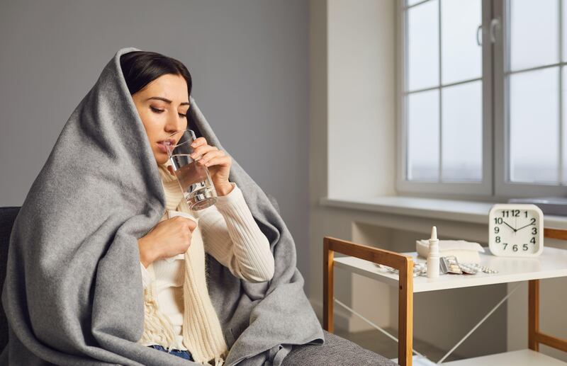 Side view of an ill young woman wrapped up in a blanket drinking water