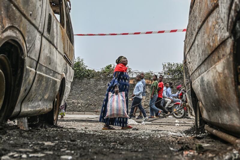 Residents walk by charred vehicles in Goma (Moses Sawasawa/AP)