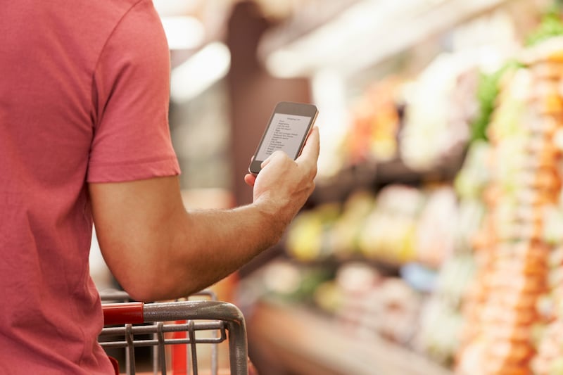 Close Up Of Man Reading Shopping List From Mobile Phone In Supermarket