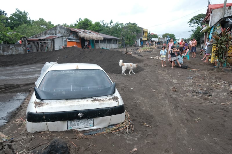 People stay beside a car partially buried by volcanic mud that had flowed down from Mayon volcano after heavy rains caused by Tropical Storm Trami (AP/John Michael Magdasoc)