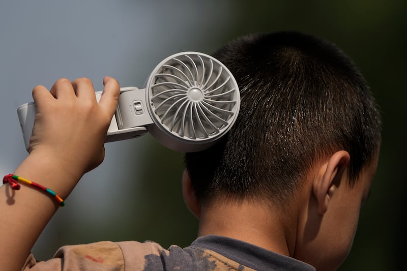 A boy cools himself with an electric fan on a sweltering day at a park in Tongzhou, on the outskirts of Beijing (AP)