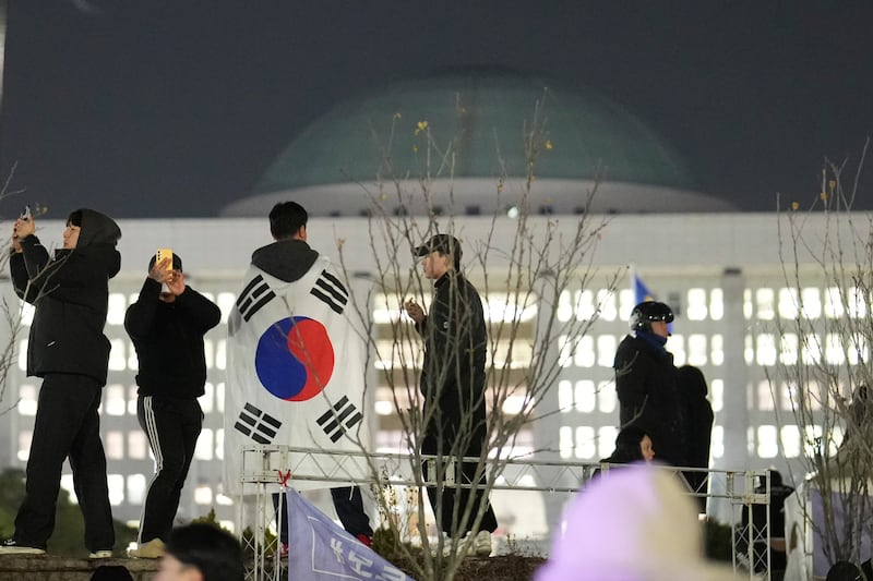 A man wearing a national flag stands on the wall of the National Assembly in Seoul (Lee Jin-man/AP)