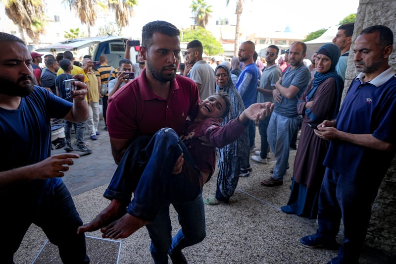 A Palestinian man carries an injured child after an Israeli air strike in Deir al Balah (Abdel Kareem Hana/AP)