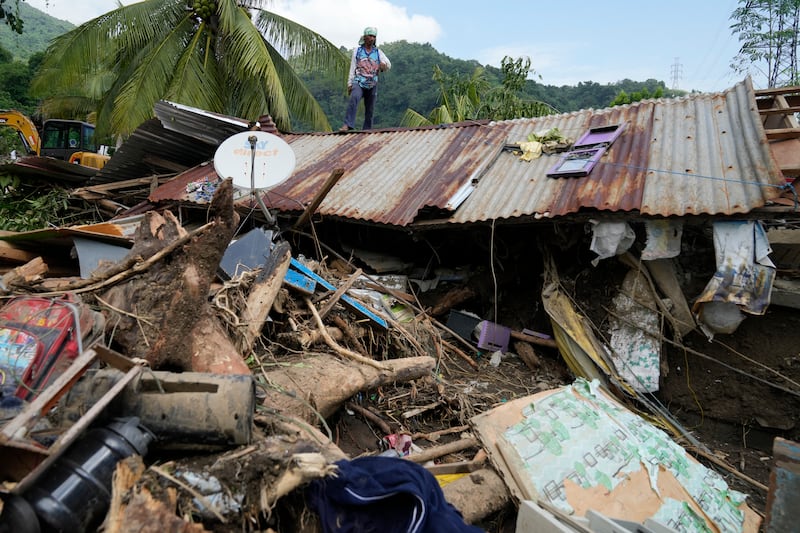 Marcelino Aringo stands on top of a damaged house after a landslide in Asia (Aaron Favila/AP)