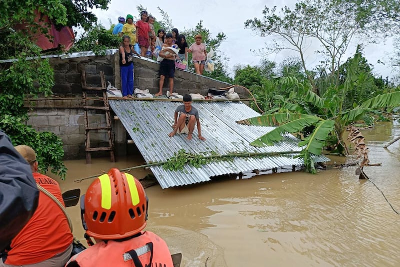 In this photo provided by the Philippine Coast Guard, people stay on top of their roofs to avoid floods caused by Tropical Storm Trami (Philippine Coast Guard/AP)