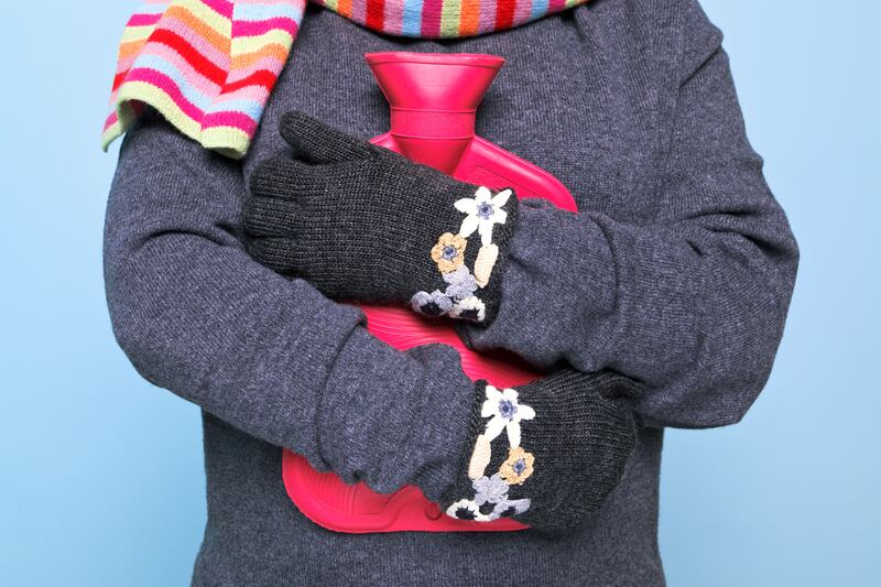 Cropped photo woman wearing a coat, gloves and scarf cuddling a red hot water bottle