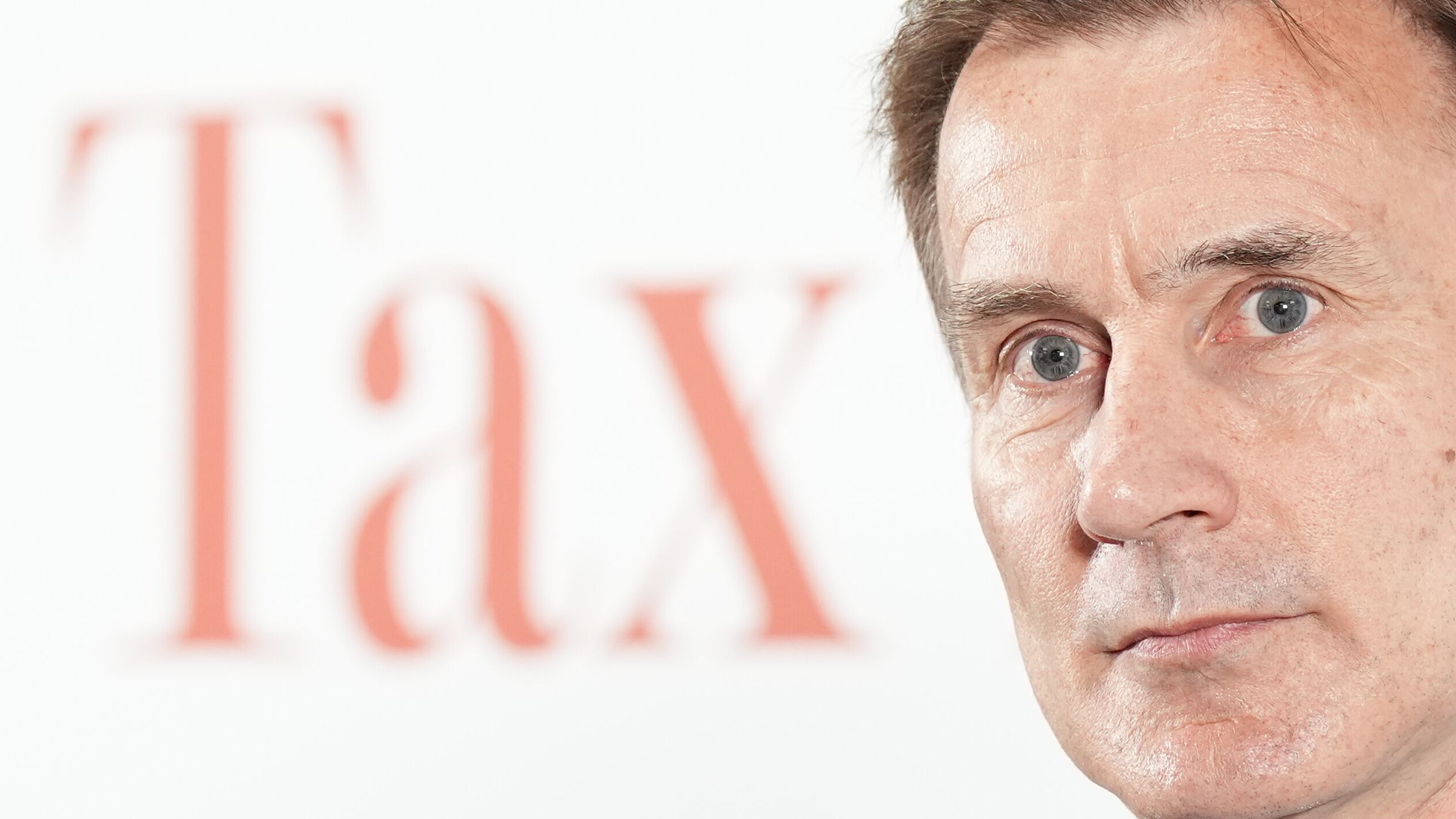 Chancellor Jeremy Hunt in front of a white background with the word ‘Tax’ on it
