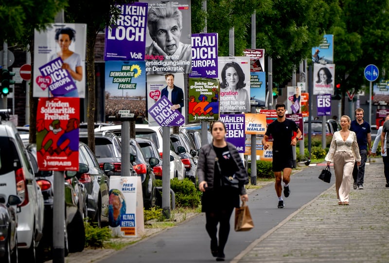 People walk past election campaign posters attached to lampposts along a street in Frankfurt, Germany (Michael Probst/AP)