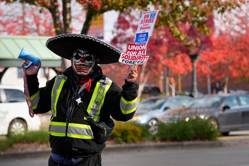 Boeing mechanic Eugenio, who preferred not to give a last name, sounds a bullhorn while holding a sign (Lindsey Wasson/AP)