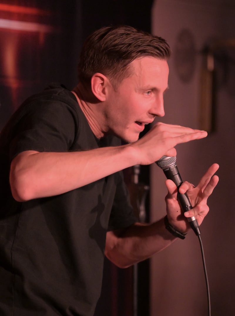 Male stand-up comedian gestures on stage while holding microphone