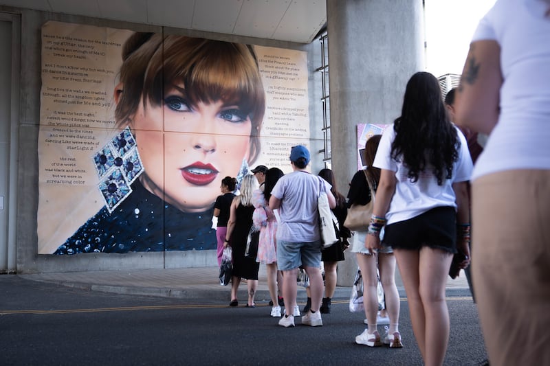 Swifties line up to pose in front of a mural outside Wembley