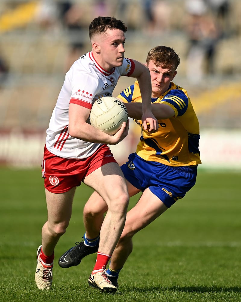 Eoin McElholm running holding a ball being held back by a player in a Roscommon GAA kit