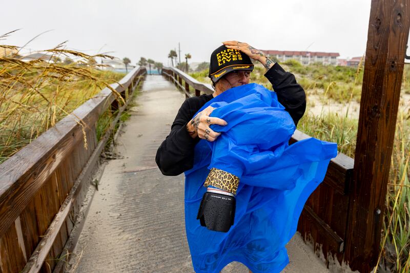 Amy Tittle holds on to her hat while trying to photograph her son surfing in the high waves created by Tropical Storm Debby near the pier in Tybee Island, Georgia