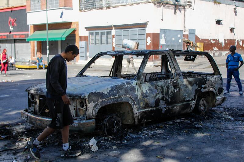 Residents stand around a vehicle burned during the previous day’s protests against official election results (Cristian Hernandez/AP)