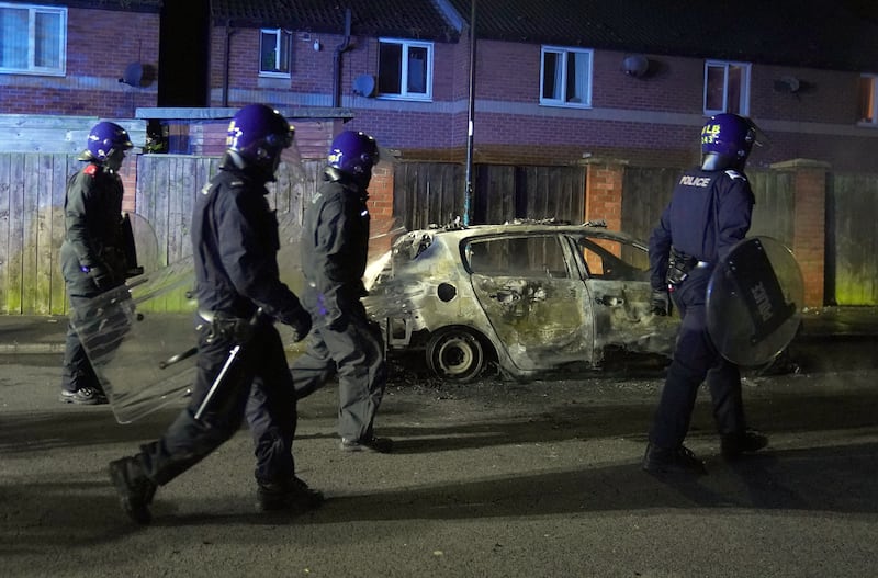 Police officers walk past a burnt out police vehicle as they are deployed on the streets of Hartlepool following a violent protest