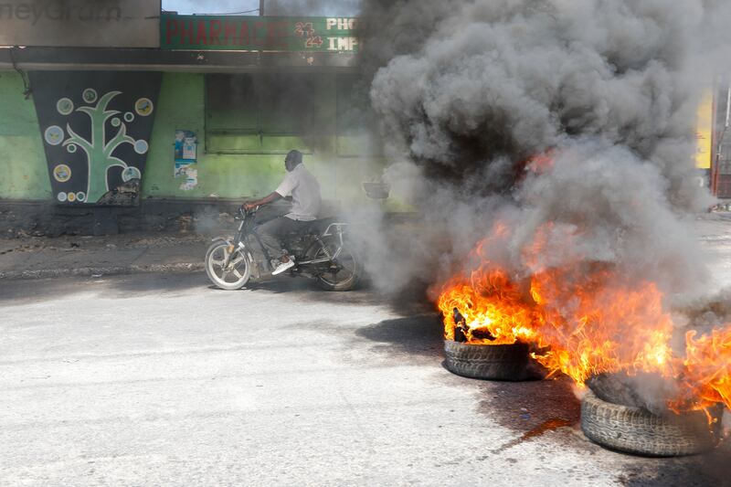 A motorcyclist rides past burning tyres (Odelyn Joseph/AP)
