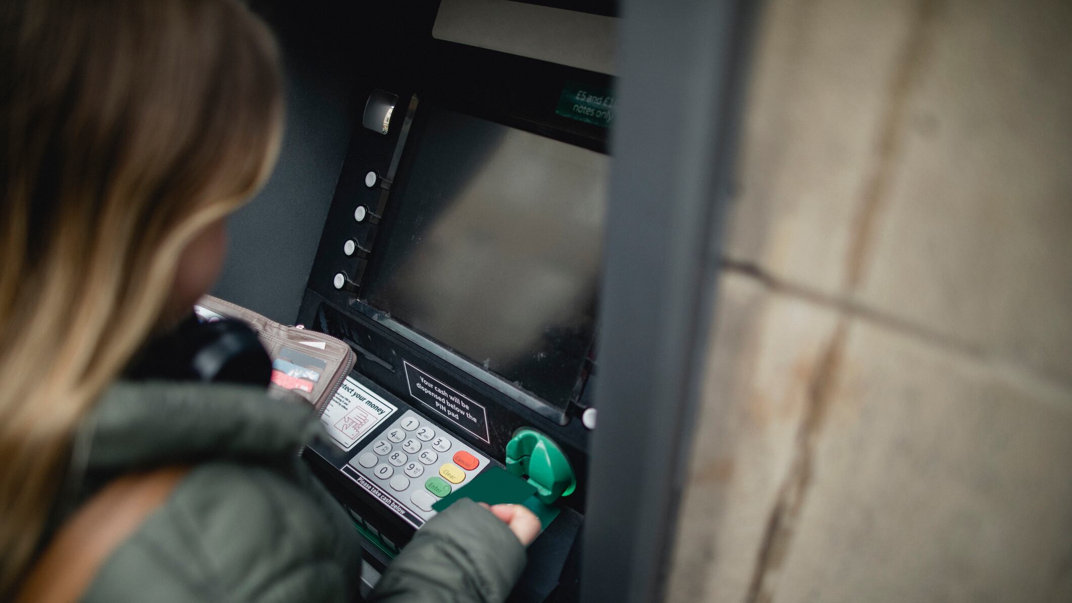 Over the shoulder view of a young female adult using a cashpoint machine.