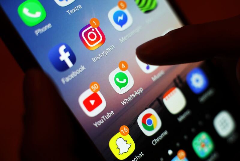 A thumb over a mobile phone screen showing various social media apps.