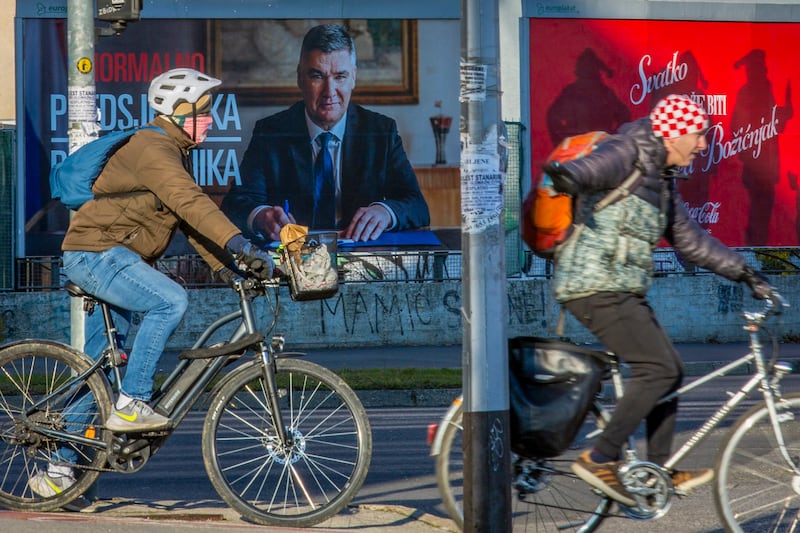 Cyclists ride past a poster of incumbent President Zoran Milanovic in Zagreb (AP)