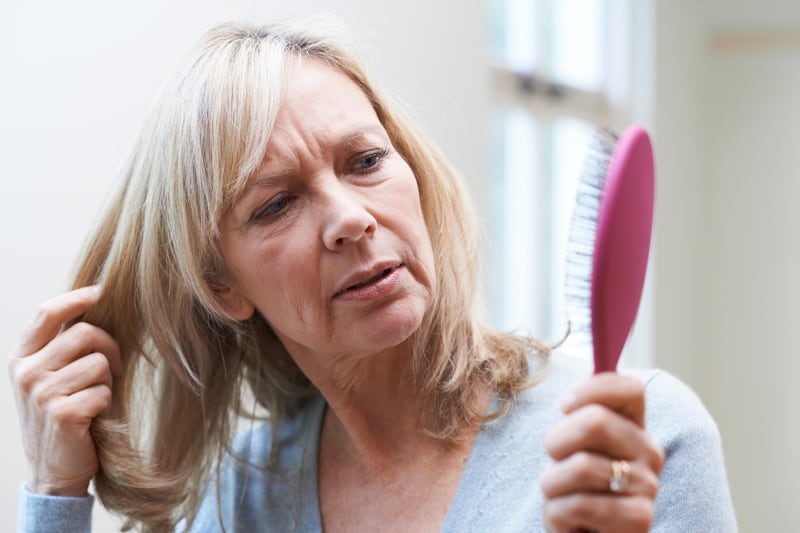 Mature woman looking at her hair brush concerned about hair loss