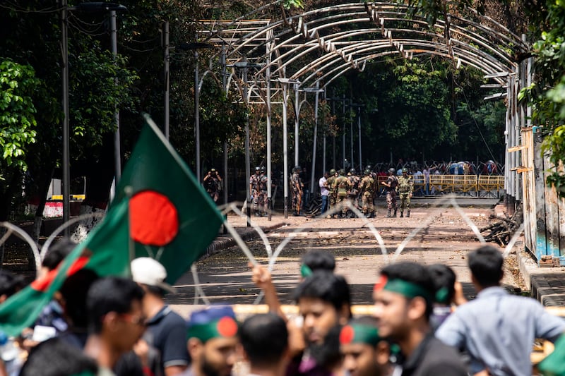 Military and paramilitary personnel stand guard as protesters block the road in front of the former residence of Sheikh Mujibur Rahman