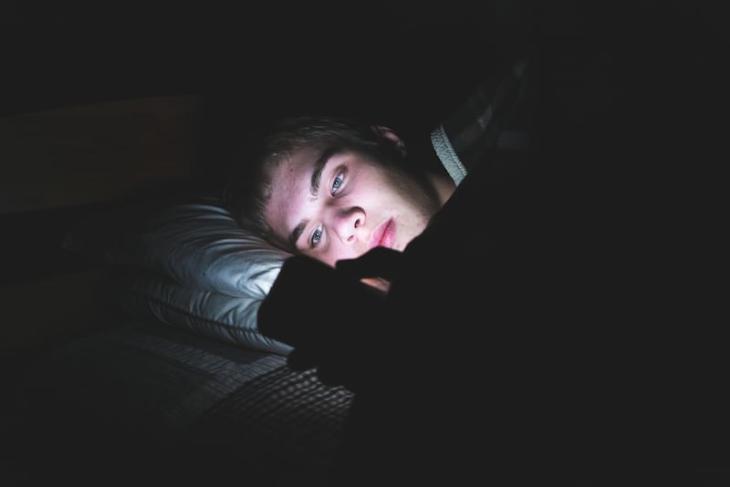 Teenage boy scrolling on his phone in bed in the dark (Alamy/PA(