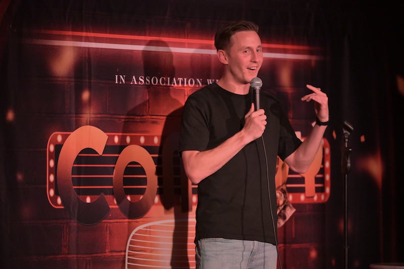 Male stand-up comedian gestures on stage while holding microphone