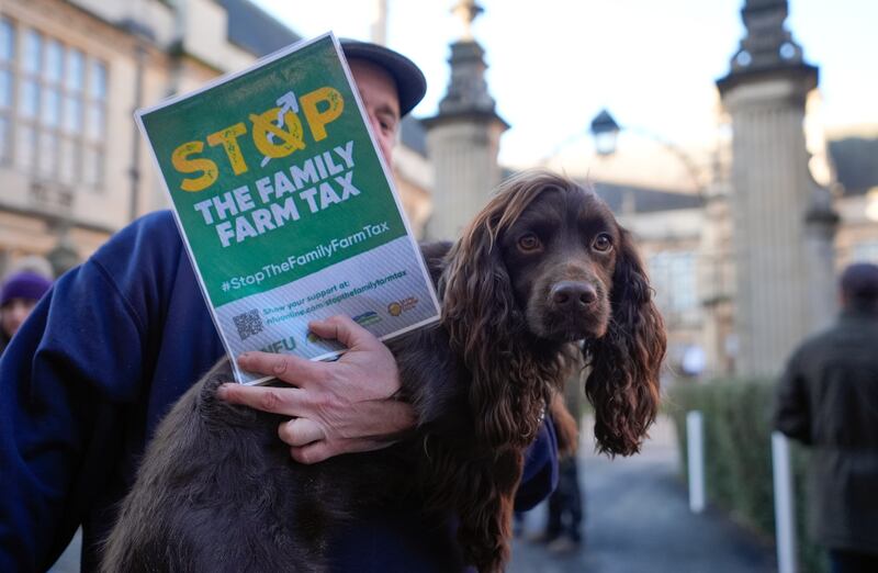 A farmer holds his dog as he takes part in a protest over the changes to inheritance tax rules outside the Oxford Farming Conference