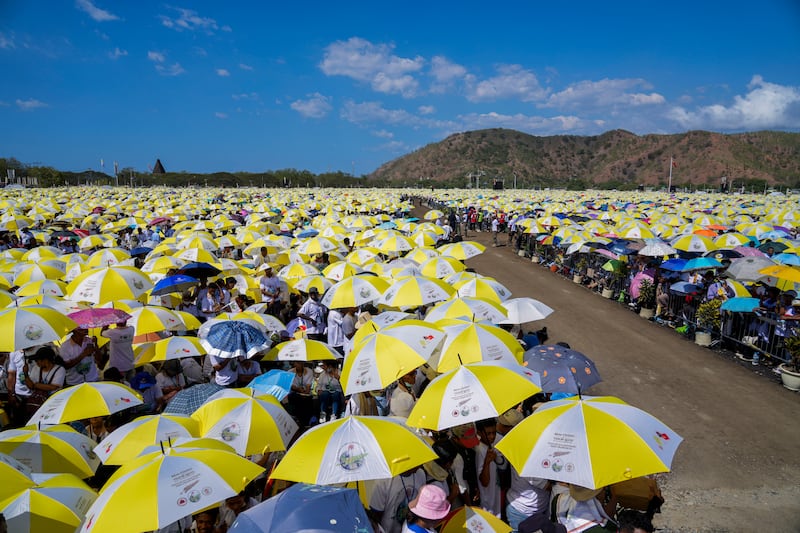 Worshippers use umbrellas in the colours of the Vatican flag to shield themselves from the sun as they wait for the Mass to start in Tasitolu Peace Park (Gregorio Borgia/AP)