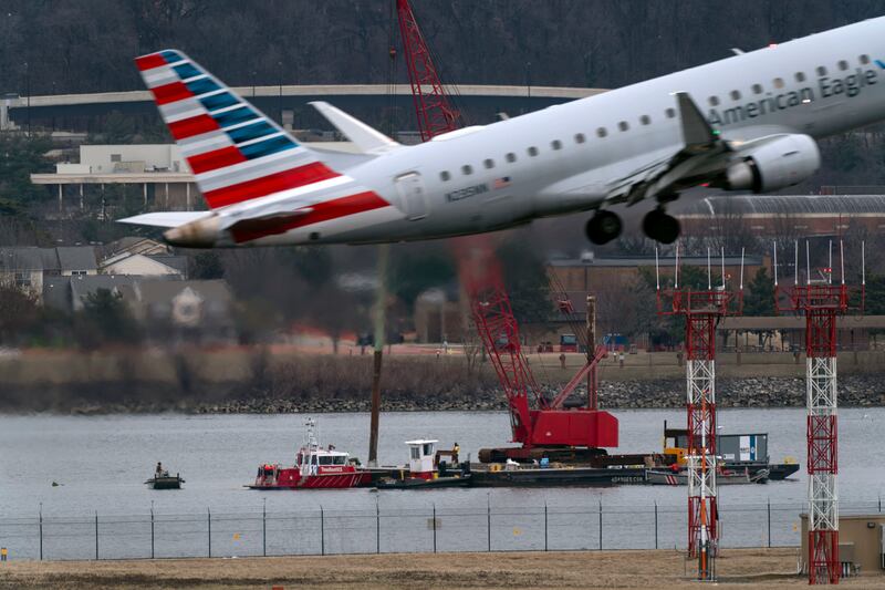 An airliner passes as rescue and salvage crews work near the wreckage in the Potomac River (Jose Luis Magana/AP)