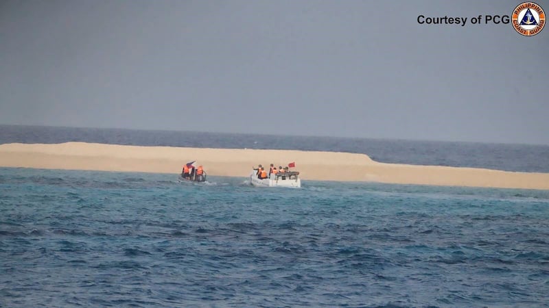 Chinese Coast Guard boat sails near Sandy Cay, seen in the background, in the South China Sea (Philippine Coast Guard via AP)