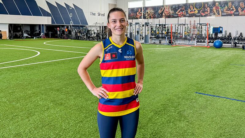 A woman standing with her hands on her hips, wearing a pred, yellow and blue-striped jersey