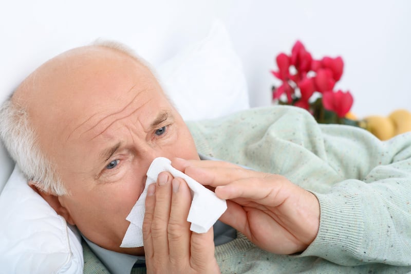 Sad old man blowing his nose into a white handkerchief