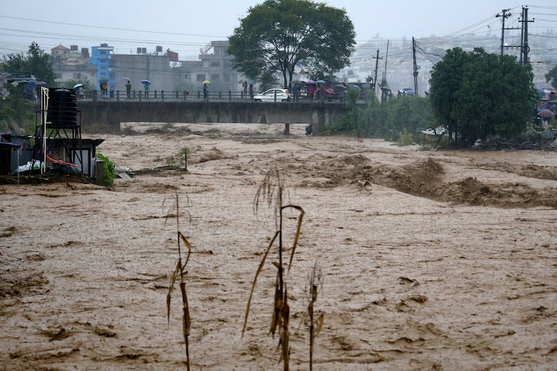 People watch the turbulent waters of Bagmati River from a bridge as the river flooded due to heavy rains in Kathmandu (Gopen Rai/AP)