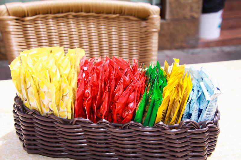 Close up of wooden basket with choice of small colorful plastic packages of sauces on table of restaurant outdoor