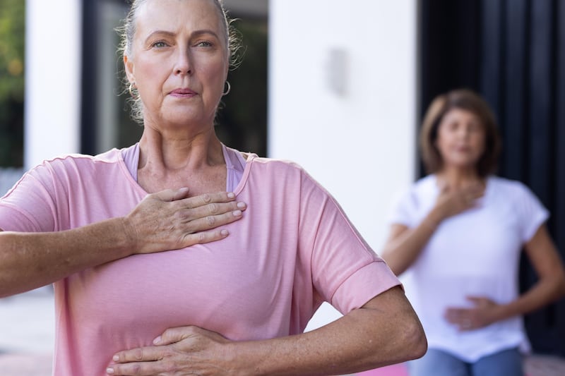 Two senior women sat on the floor with one hand on their chest doing breathing exercises together