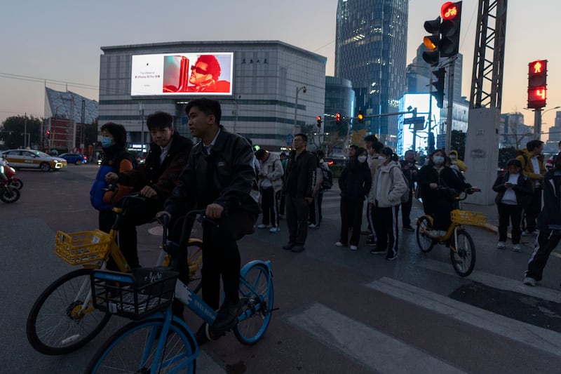 Pedestrians and cyclists wait to cross a traffic junction near a advertisement for iPhones in Beijing (Ng Han Guan/AP)