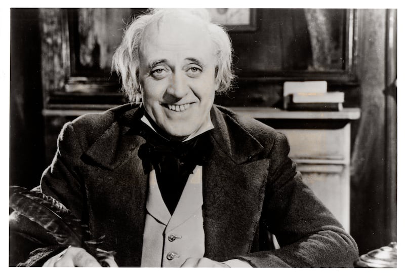 Black and white image of actor Alastair Sim, as Scrooge, smiling.