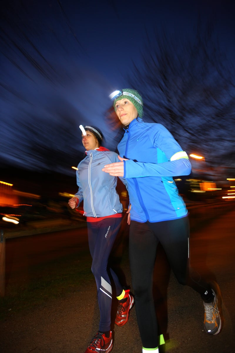 Two young women wearing reflective clothing jogging together at night