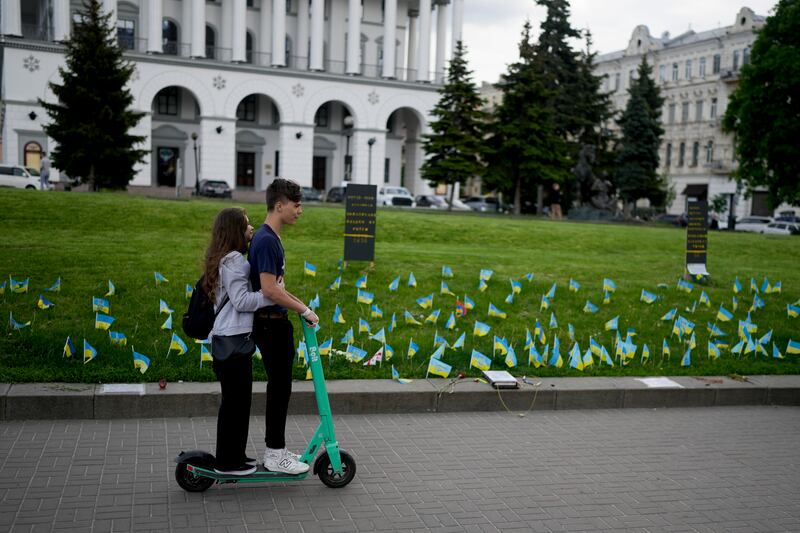 A couple ride a scooter in front of flags in Independence Square honouring soldiers killed fighting Russian troops (Natacha Pisarenko/AP)