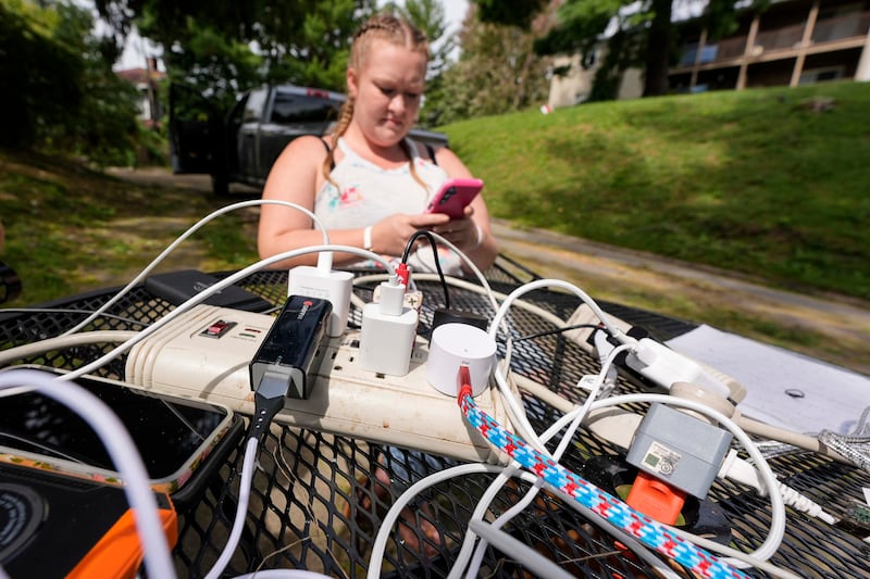 A woman looks at her phone as an Asheville resident with power drops an extension cord for others to use (Mike Stewart/AP)