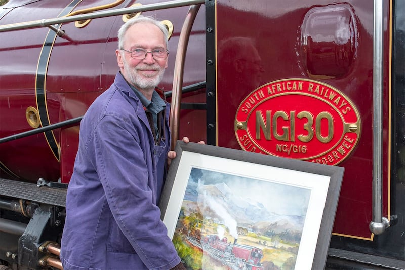 Steam engine restoration enthusiast Peter Best smiling while standing next to a train and holding a framed painting of a train