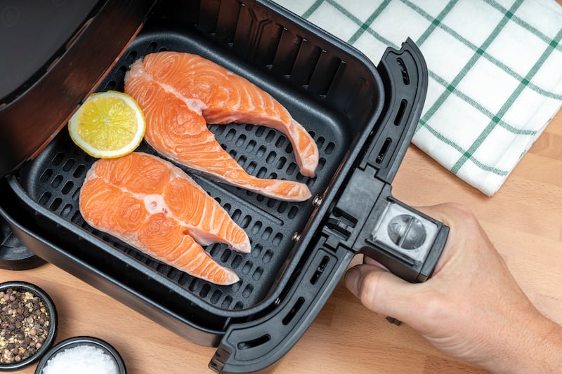 HAND HOLDING AIR FRYER BASKET WITH TWO SLICES OF RAW SALMON READY TO COOK IN THE KITCHEN. TOP VIEW.