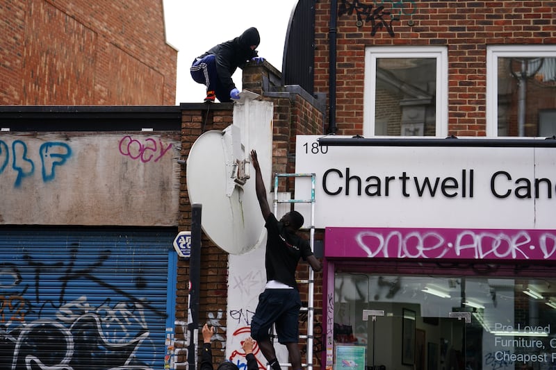 People remove a new artwork by Banksy, a howling wolf painted on a satellite dish