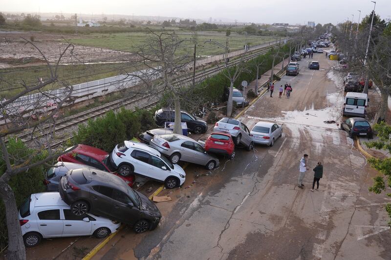 Residents walk next to cars piled up after being swept away by floods in Paiporta (Alberto Saiz/AP)