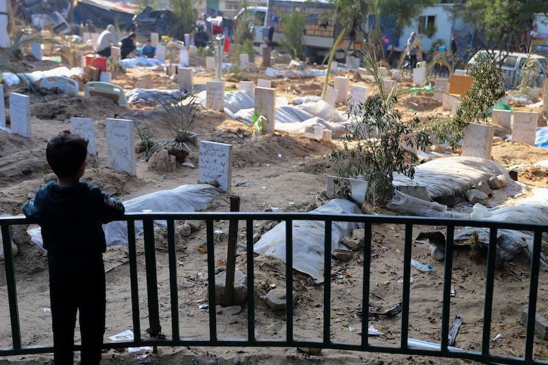 A Palestinian child looks at the graves of people killed in the Israeli bombardment of the Gaza Strip and buried inside the Shifa Hospital grounds (Mohammed Hajjar/AP)