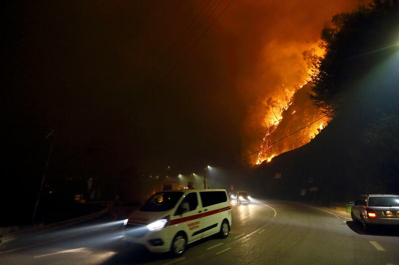 Vehicles drive past a fire burning by the road near a town in northern Portugal (Bruno Fonseca/AP)