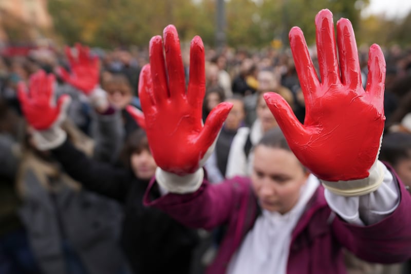 Protesters shout slogans with red paint on their hands (Darko Vojinovic/AP)