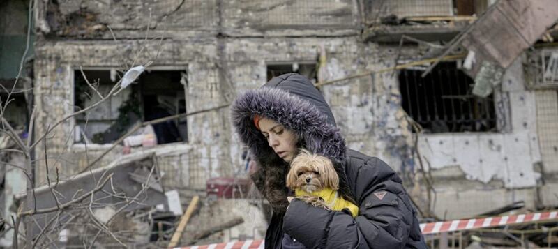 A woman holding a small dog walks in front of an apartment in a block which was destroyed by an artillery strike in Kyiv, Ukraine, yesterday. Picture by Vadim Ghirda, Associated Press 